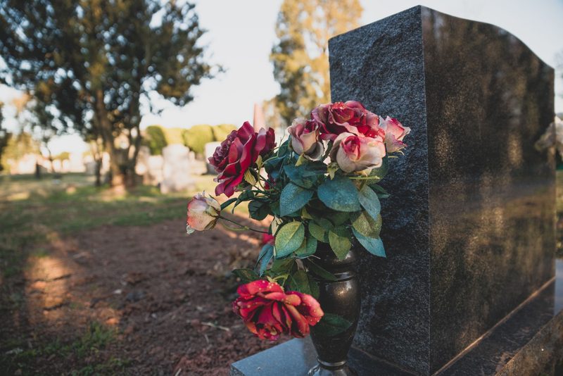 Gepflegte Grabstätte mit dunkelroten Rosen an einem hellen Grabstein